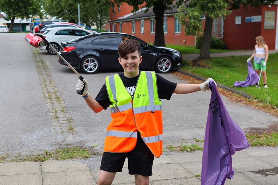A young volunteer posing for the camera as he helps litter pick in the community. He is holding a bag for litter 