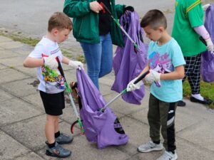 Two young people helping each other pick up litter by holding a bag open for them