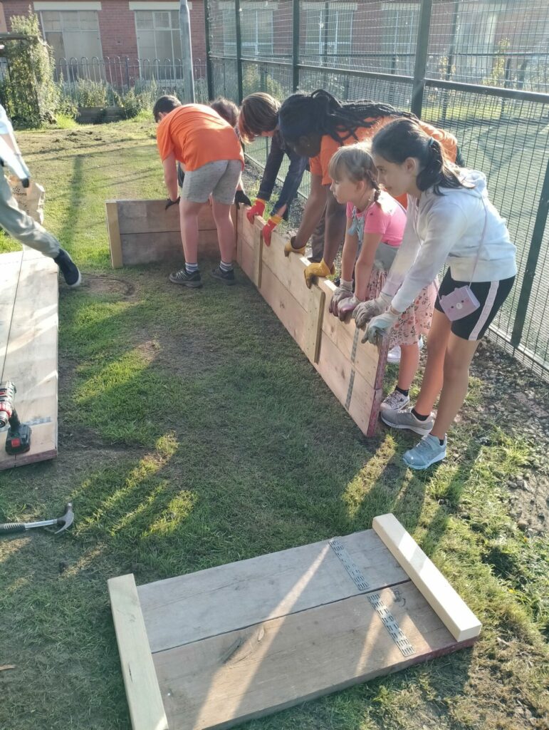 A group of young people holding a plank of wood, preparing to put different pieces of an outdoor planter together
