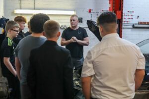 The Mechanics course at The Hunslet Club. A group of students standing and listening to the mechanics tutor as they look at the engine of a car.