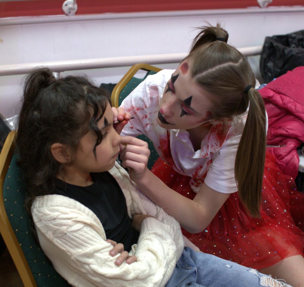 Two young people helping paint each others faces to look like clowns 