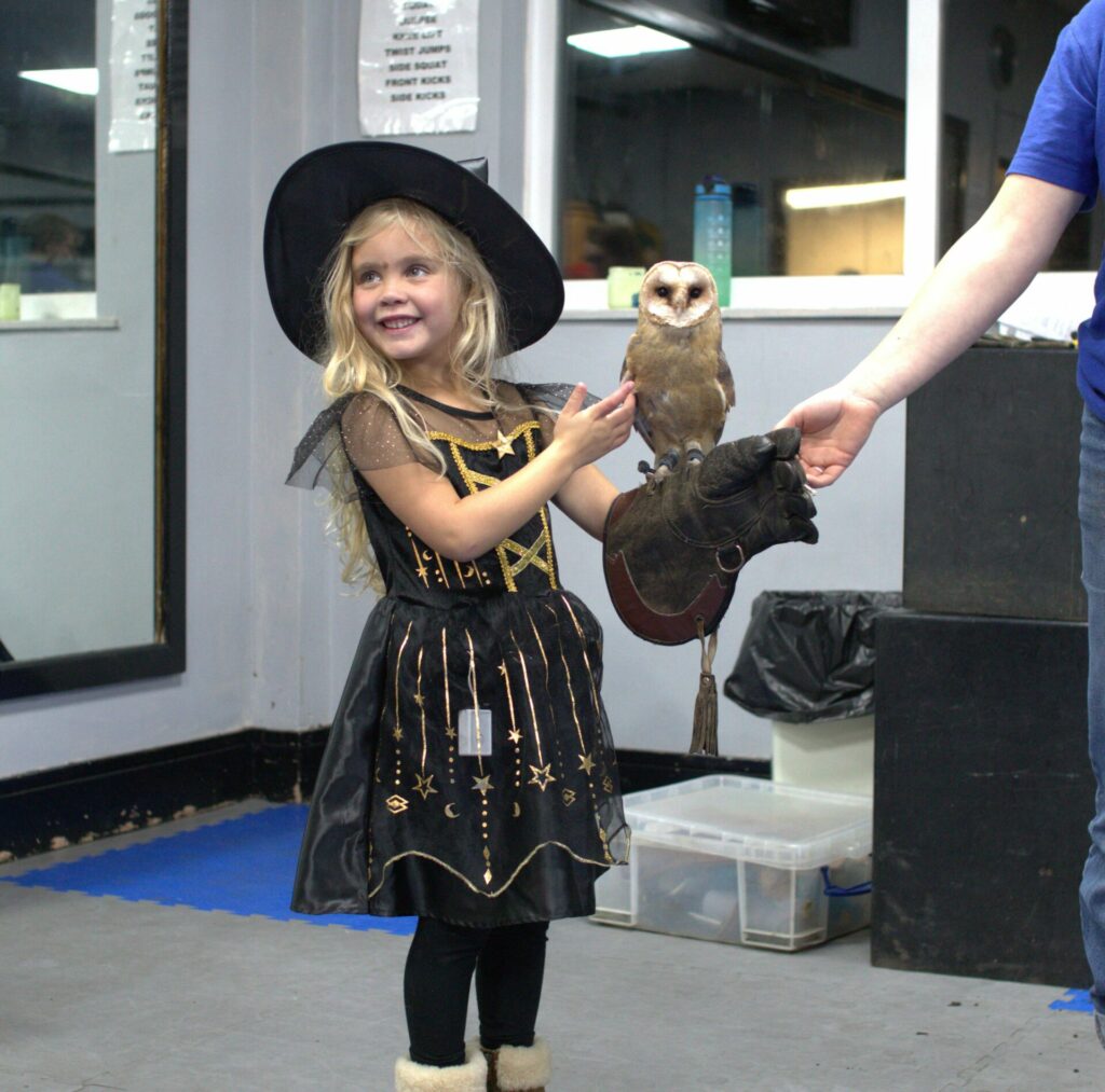 A little girl dressed as a wtich holding a barn owl