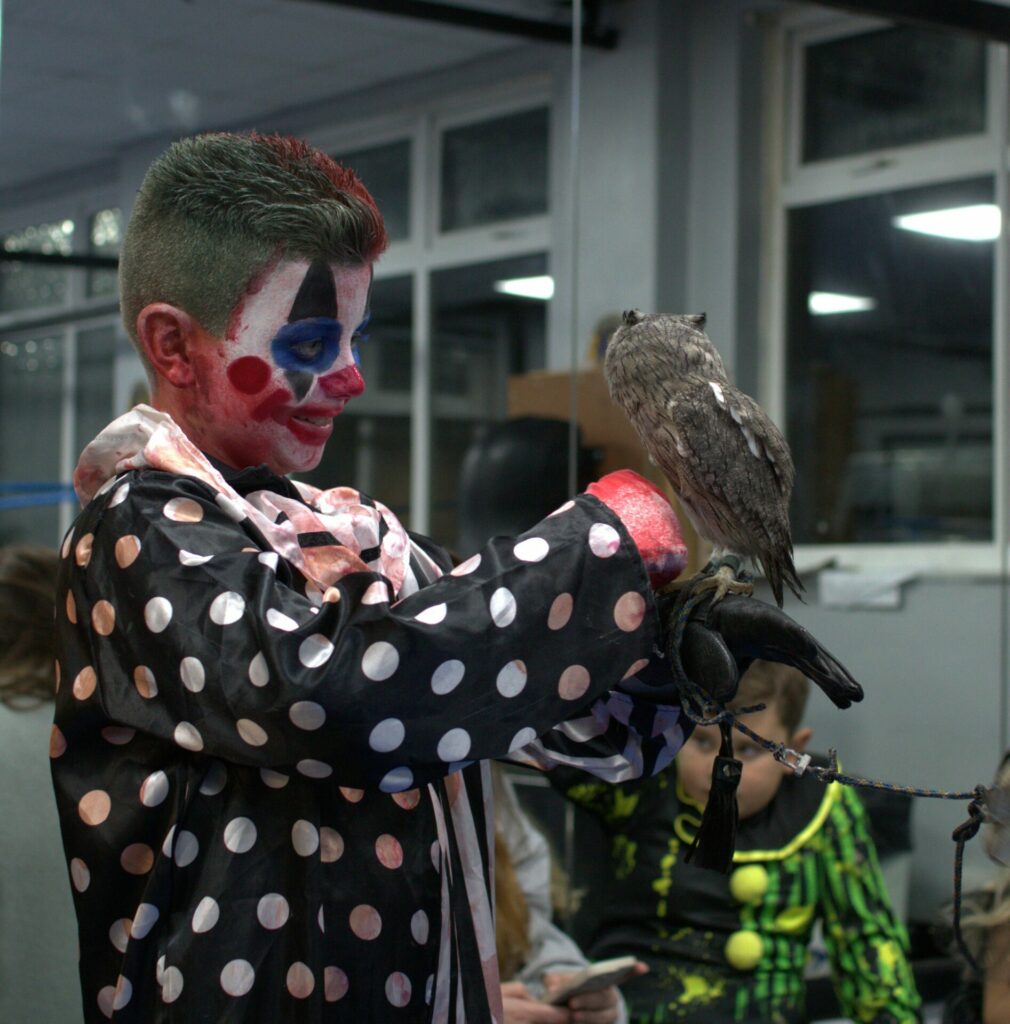 A young person dressed as a clown, holding an owl. 