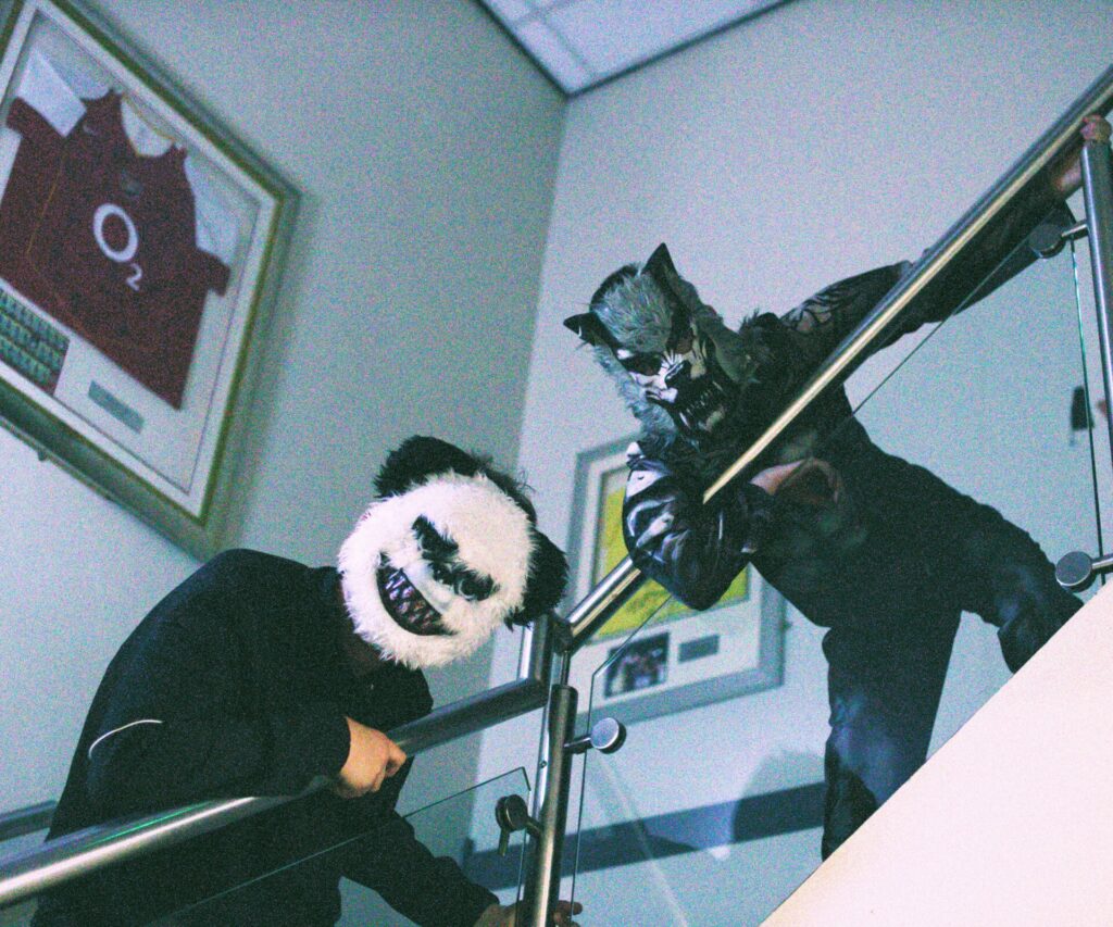 Two young people wearing masks looking down from stairs in a scary manner. 