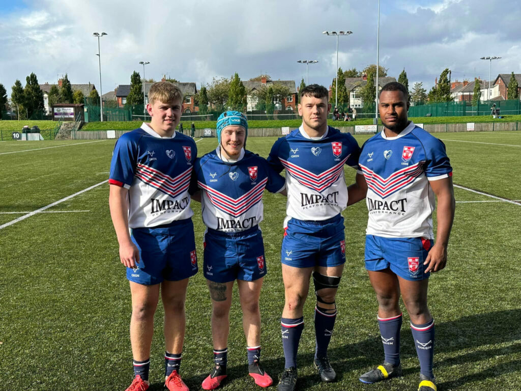 Four Rugby players standing on a field - all dressed in Rugby kit. 